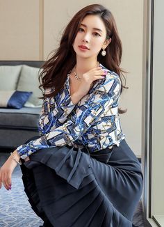 Woman with long hair wearing a patterned blouse and pleated skirt indoors