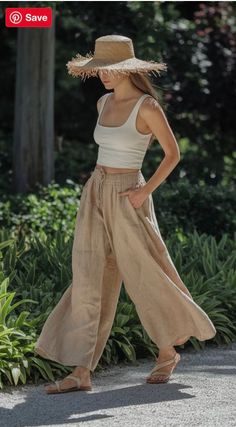 Woman in a straw hat, crop top, and wide leg pants walking outdoors