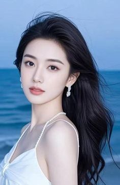 Woman with long black hair wearing a white dress and pearl necklace outdoors
