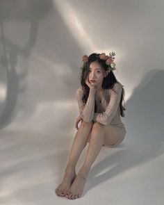 Woman with a flower crown and beige dress sitting barefoot indoors