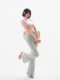 Woman with short black hair in a pink top and flared jeans posing on white background
