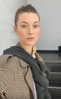 Woman with a hair bun and freckles wearing a houndstooth jacket indoors
