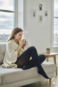 Woman wrapped in a blanket, drinking from a mug on a sofa indoors