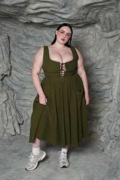 Woman in an olive green dress with a laced bodice and sneakers in a studio