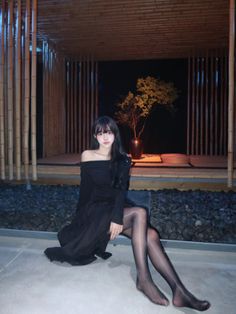 Woman in a black off-shoulder dress and pantyhose sitting outdoors at night