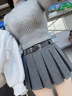 Woman in a grey ribbed sweater and pleated skirt with exposed thighs