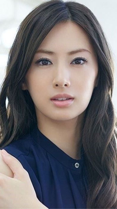 Woman with long dark hair wearing a navy blue shirt, looking directly at the camera