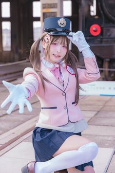 Woman in a pink blazer and school uniform kneeling at a train station