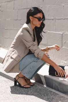 Woman in a plaid blazer and jeans crouching outdoors