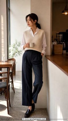 Woman in a white shirt and sweater vest holding a mug in a cafe