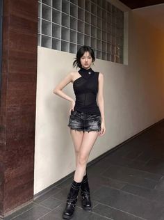 Woman in a black top, denim shorts, and black boots standing indoors