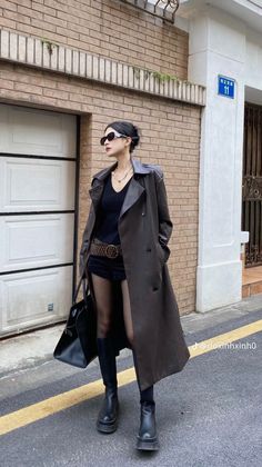 Woman in a leather trench coat, black shorts, and platform boots on a street