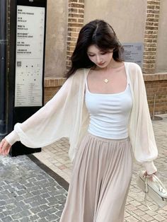 Woman with long dark hair wearing a white tank top and sheer cardigan outdoors