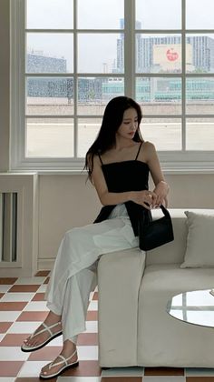 Woman with long black hair sitting on a couch by a window