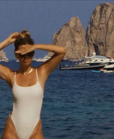 Woman in a white swimsuit shielding her eyes on the ocean with boats and rock formations