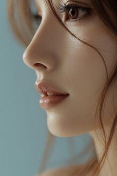 Close up of a woman's face with glossy lips and long eyelashes against a blue background