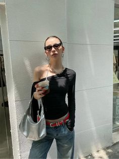 Woman in an off-shoulder top, jeans, and sunglasses holding a drink outdoors