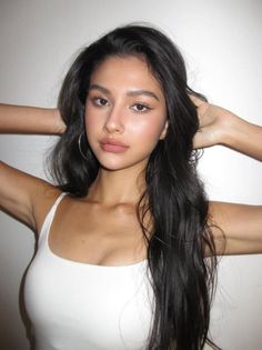 Woman with long dark hair wearing a white tank top and hoop earrings