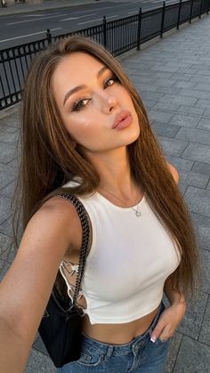 Woman with long hair in a white crop top and jeans on a street at golden hour