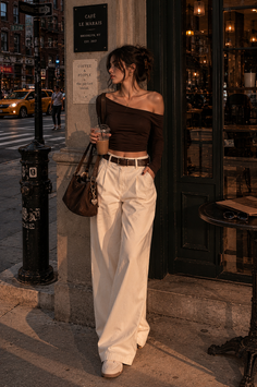 Woman in an off-shoulder top and wide-leg pants on a city street at golden hour