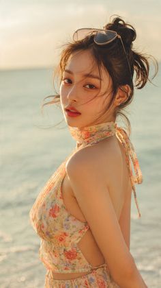 Woman in a floral dress with a messy bun and sunglasses on her head at the beach