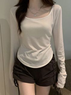 Person in a white long sleeve shirt and black shorts with a silver necklace