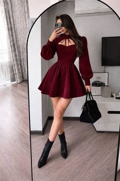Woman in a red dress and black boots taking a mirror selfie indoors