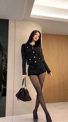 Woman in a black tweed jacket and shorts with tights and high heels indoors