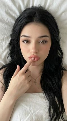 Woman with black hair and a cross necklace, finger on her lips