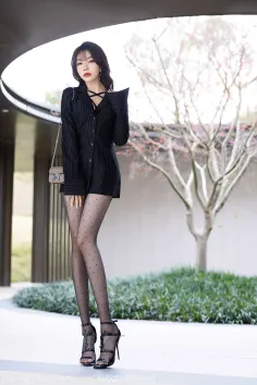 Woman in a black shirt dress and polka dot stockings posing outdoors