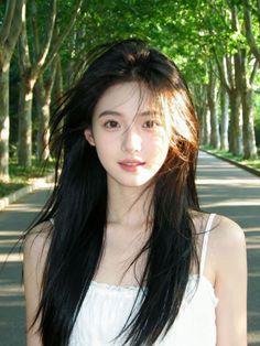 Woman with long dark hair in a white top on a tree-lined road
