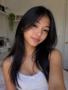 Woman with long black hair wearing a white tank top with lace trim indoors