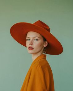 Woman in an orange wide-brim hat and shirt against a green background