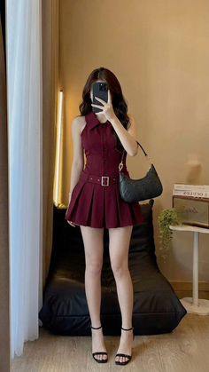 Woman in a maroon pleated dress and high heels taking a mirror selfie