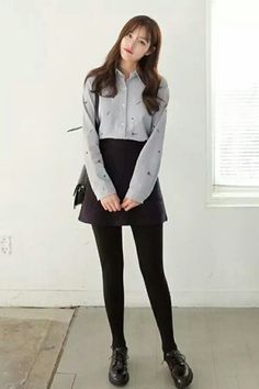 Woman with long hair wearing a collared shirt, mini skirt, and black tights indoors