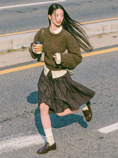Woman with long hair running across a street, holding a coffee cup