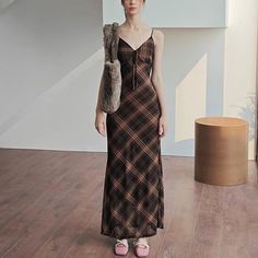 Woman in a plaid maxi dress with a furry bag and pink shoes indoors