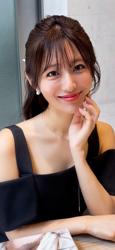 Woman in a black dress with long hair and bangs, smiling at the camera