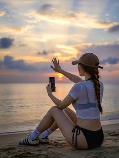 Woman in a bikini bottom and cropped top sitting on a beach at sunset