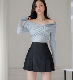 Woman with long dark hair wearing an off-shoulder top and pleated skirt indoors