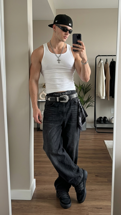 Man in a white tank top and baggy jeans taking a mirror selfie