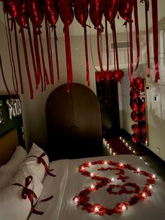 Bedroom decorated with red heart balloons, rose petals, and candles for a romantic occasion