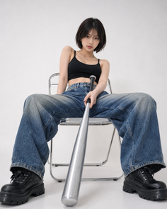 Woman with short hair in a black crop top and baggy jeans holding a baseball bat