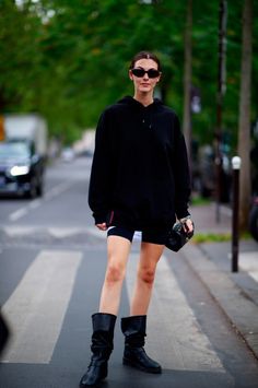 Woman in a black hoodie, cycling shorts, and boots on a street