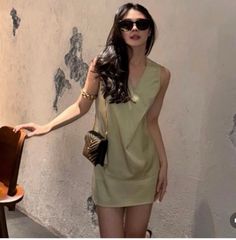 Woman in a light green mini dress and sunglasses posing indoors