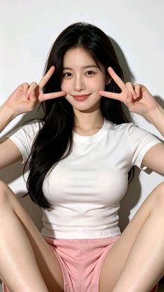 Woman with long black hair in a white t-shirt and pink shorts making peace signs