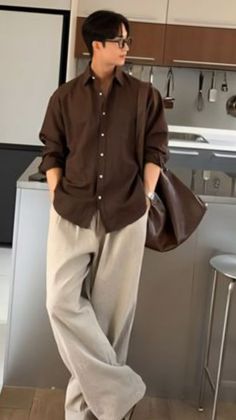 Man in a brown shirt and wide leg pants with a shoulder bag indoors