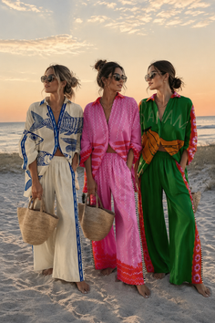 Three women in colorful matching outfits and sunglasses on a beach at sunset