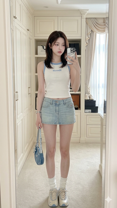Woman in a white tank top and denim mini skirt taking a mirror selfie indoors