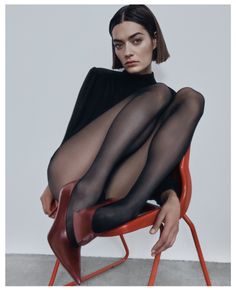 Woman with short hair in black tights and red heels sitting on a red chair